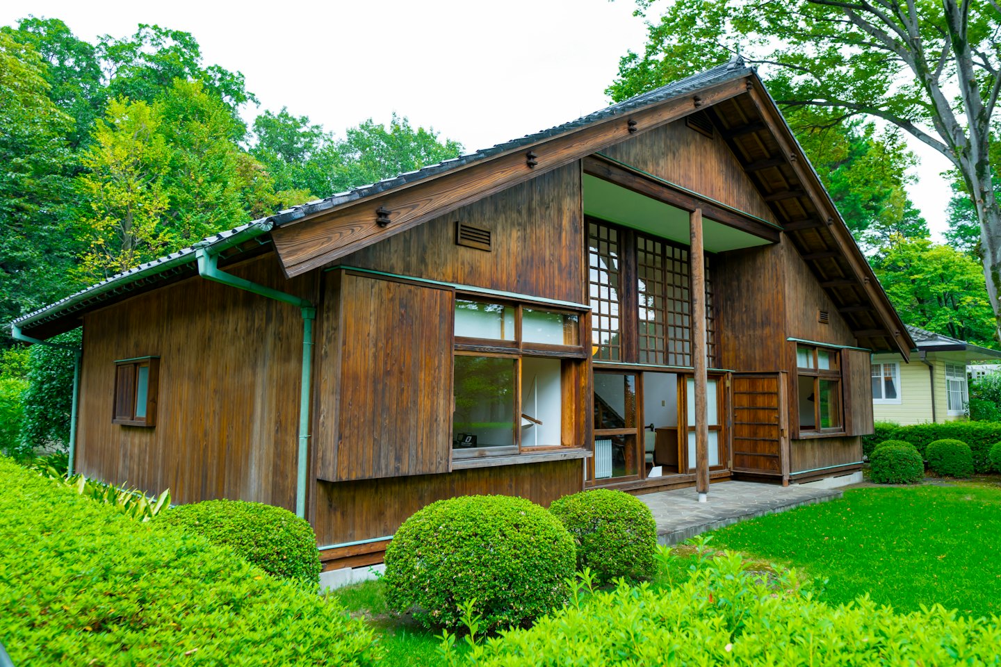 緑に囲まれた、瓦屋根と黒い木材の伝統的な日本家屋。